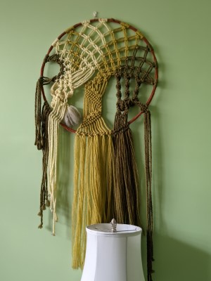 Macrame Art - by Sandra Burns ART - inspired by nature, a brown circle with knotted cords of cream, green and dark green, and long dangling cords beneath, macrame wall hanging